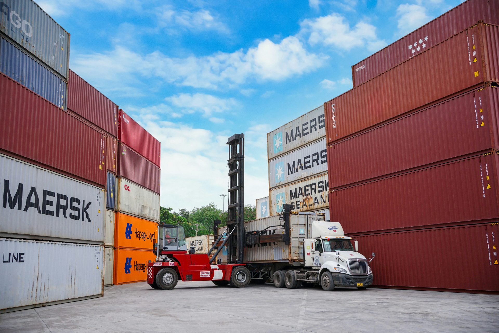 Carretilla elevadora moviendo contenedores de transporte en un puerto.